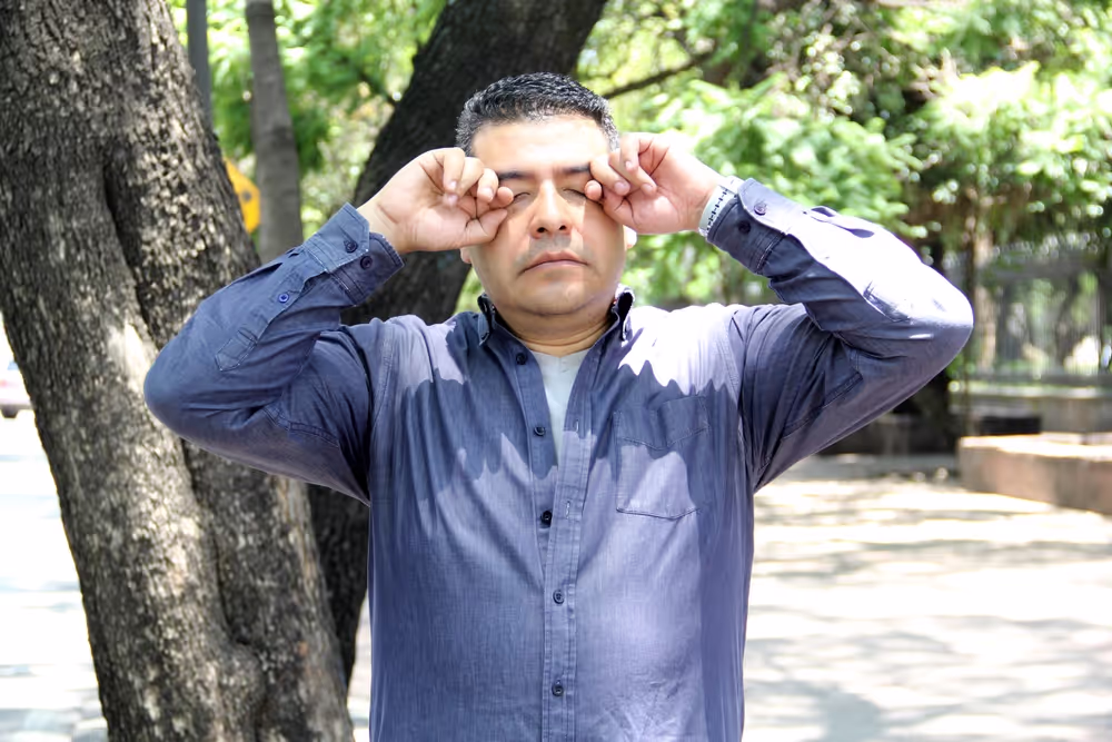 Man outdoors rubbing eyes
